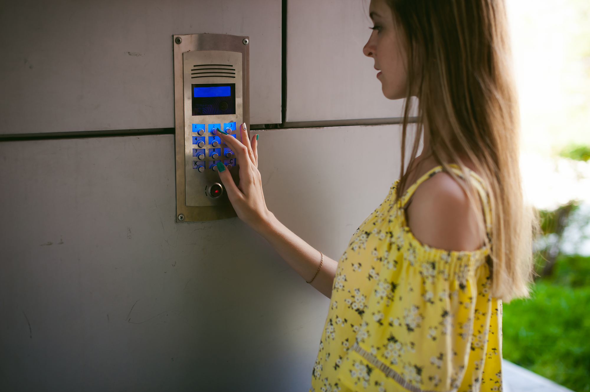 woman dials an apartment code on an electronic doorphone panel