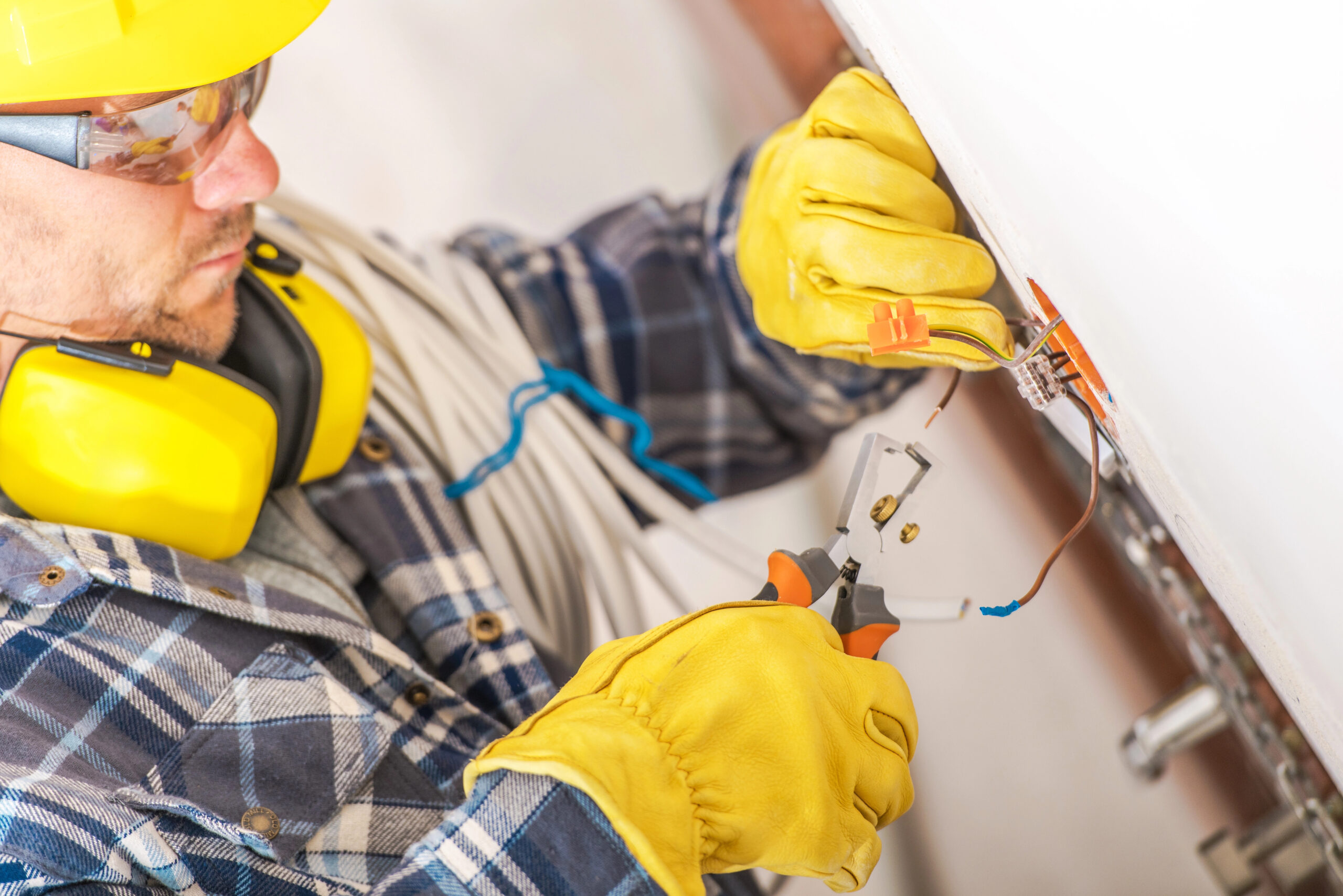 A skilled electrician is focused on connecting electrical wires while wearing protective gear and working diligently in a bright residential environment.